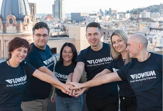 Six team members wearing Flowium T-shirts standing together on a rooftop, smiling and placing their hands together.